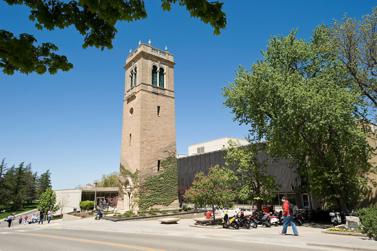 Trees and pedestrians frame a view of the Carillon Tower in front of the Sewell Social Sciences Building