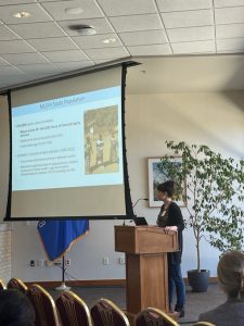 A person standing behind a podium and presenting with a screen behind them.