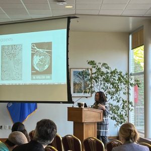 A person standing behind a podium and presenting with a screen behind them.