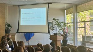A person standing behind a podium and presenting with a screen behind them.